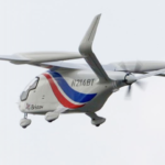 White small aircraft in flight with red and blue swoosh branding and Bristow logo, tail number N214BT, propeller spinning under a cloudy sky